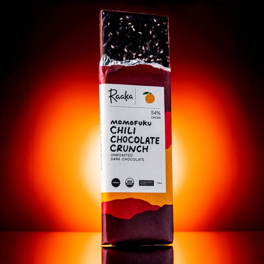 Chili Chocolate Crunch bar popping out of wrapper. Bar is garnished with salt and sesame seeds and has puffed quinoa. 