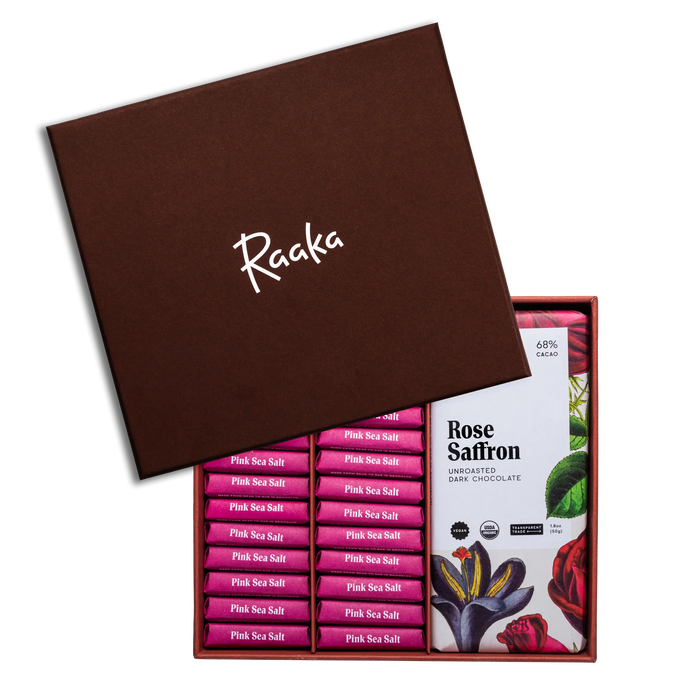 Open box of Raaka chocolate bars with a focus on 'Rose Saffron' flavor packaging.